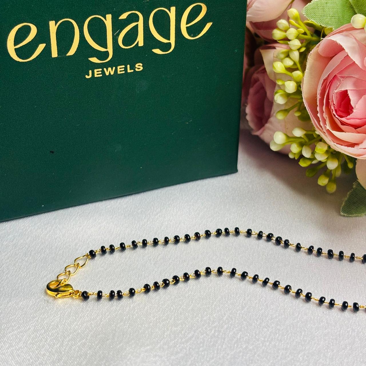 Necklace with black beads and gold clasp on a white surface with 'engage jewels' branding in the background.